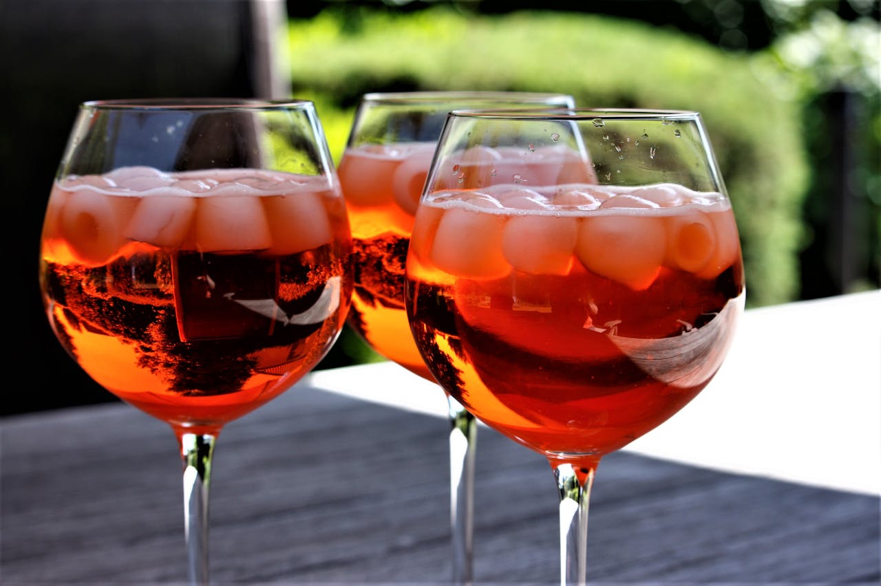 Three chilled cocktail glasses filled with a vibrant orange drink and ice cubes on a sunny day.