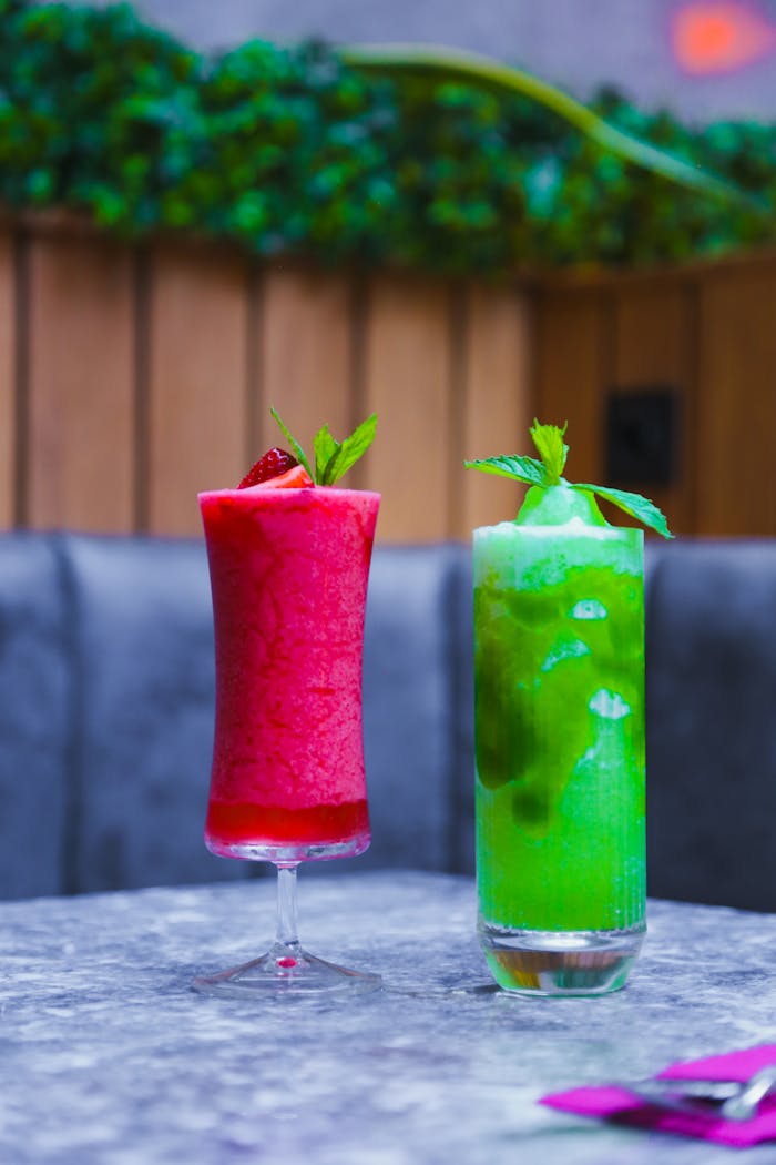 Vibrant red and green fruity drinks with mint served in long glasses on a table.